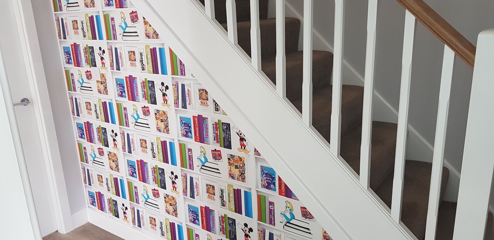 A staircase wall papered in a bright book-spine feature wallpaper