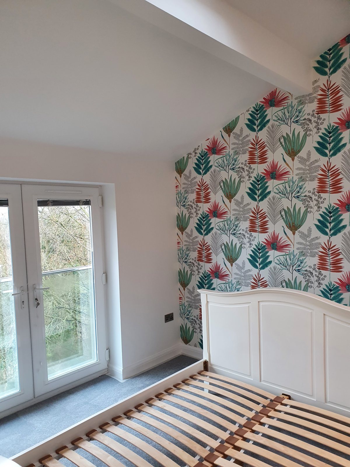 A bedroom feature wall in a tropical leaf wallpaper beside white walls