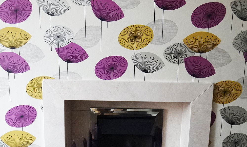 A fireplace wall papered in a dandelion-print wallpaper